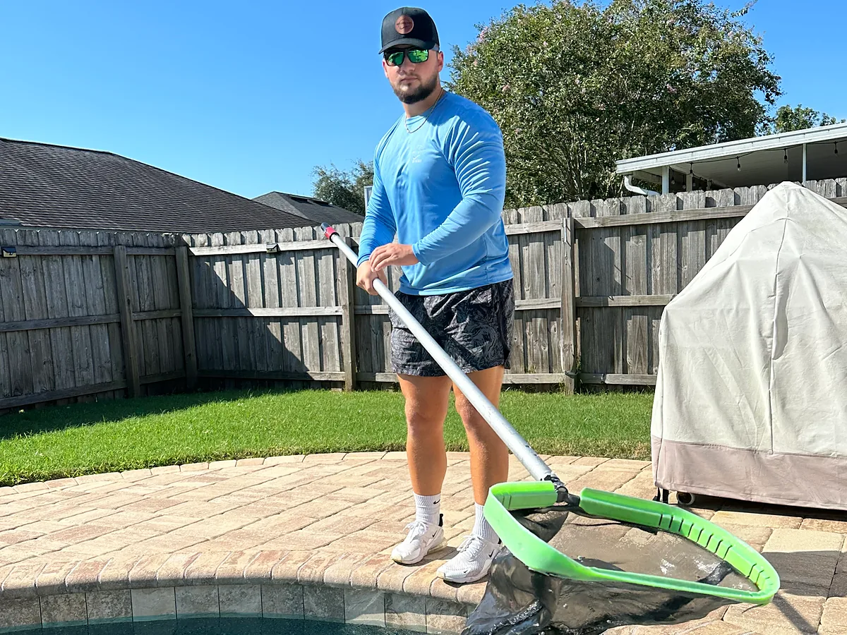 Pool tech skimming a backyard pool with a leaf net