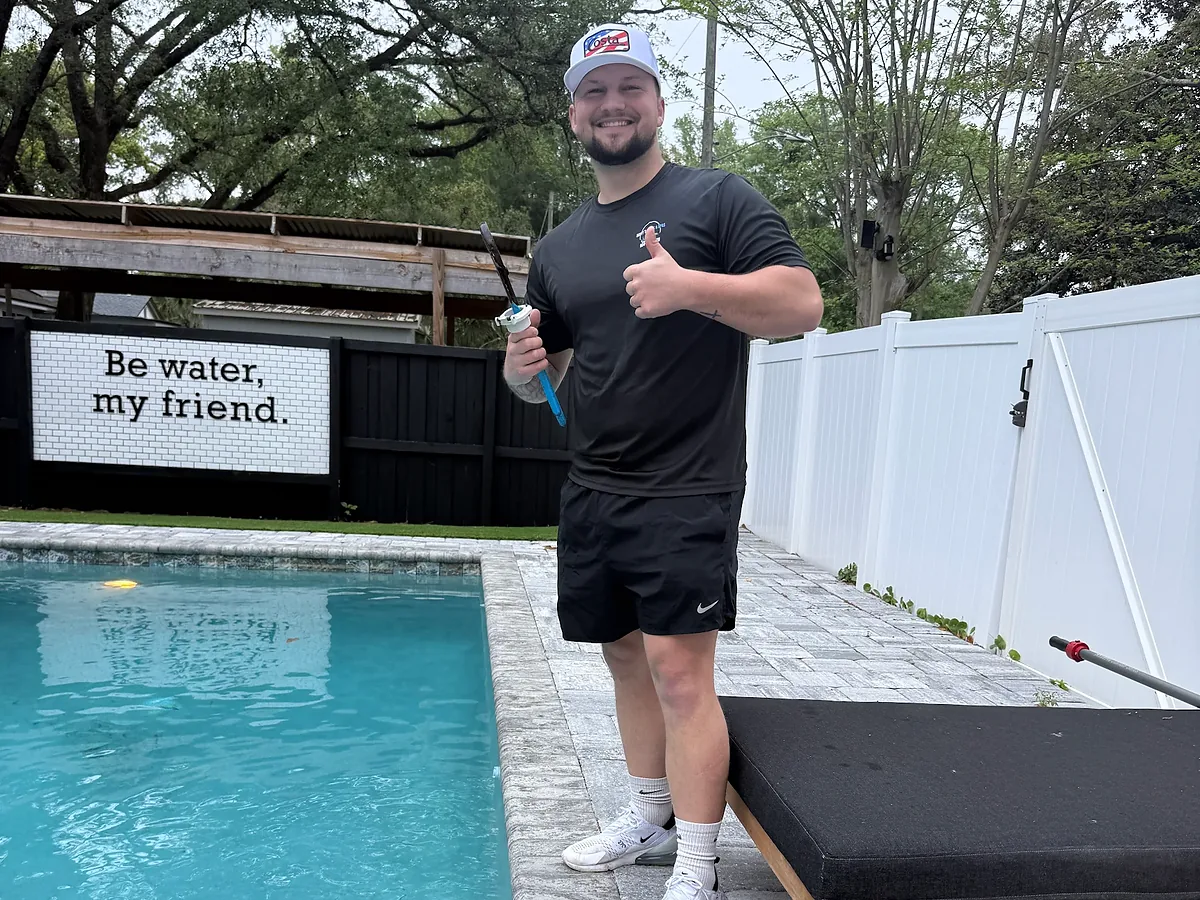 Pool tech giving a thumbs up beside a clean backyard pool
