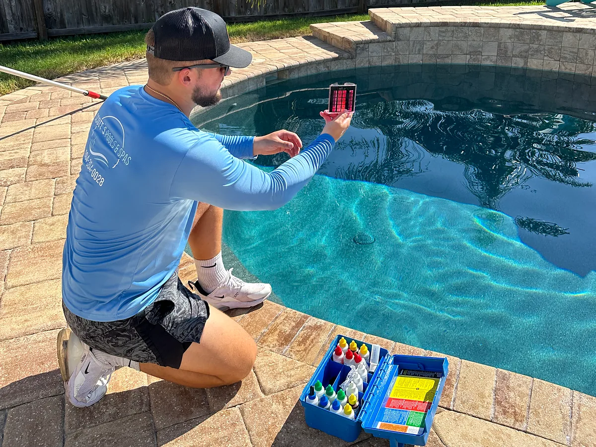 Pool tech checking pool water with a test kit beside the pool